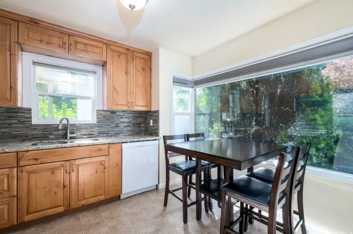 Wood-finish cabinetry, tile backsplash, stainless-steel sink, and a built-in dishwasher
