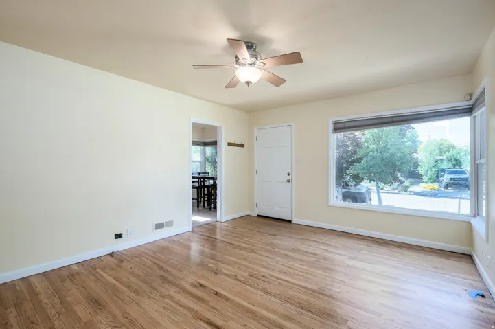 Wood-finish flooring, ceiling fan with integrated lighting, large picture window, and paneled entry door
