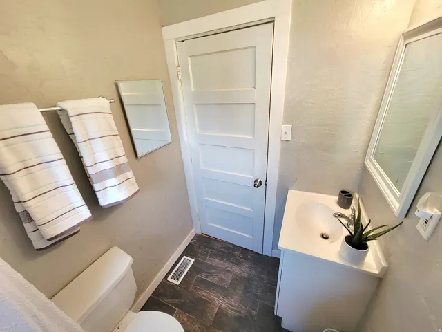 White panel door, wood-finish flooring, white vanity with integrated sink, chrome faucet, and framed wall mirror