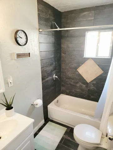 Bathtub with tile surround, a single window, and a white vanity with an integrated sink