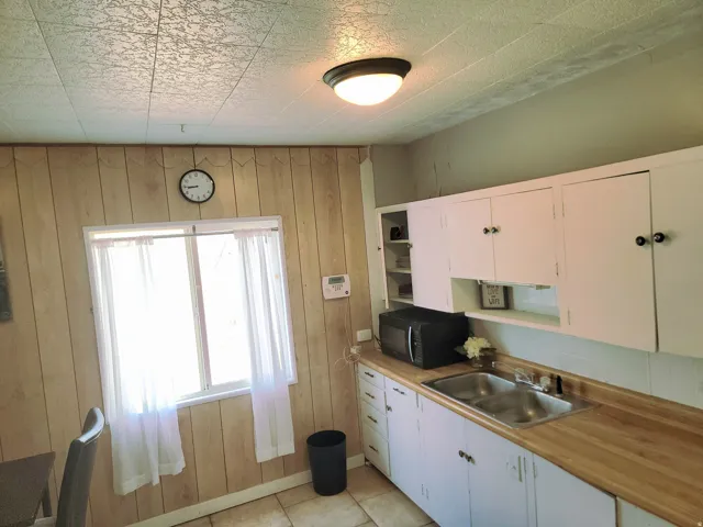 White upper and lower cabinetry with black hardware, wood-finish countertops, and a dual stainless steel sink