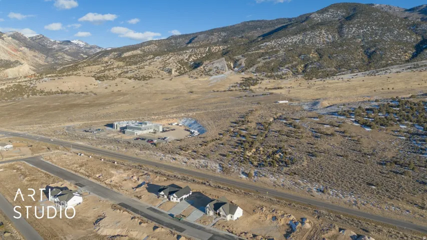 Expansive development land featuring a paved road, mountain backdrop, and multiple residential structures