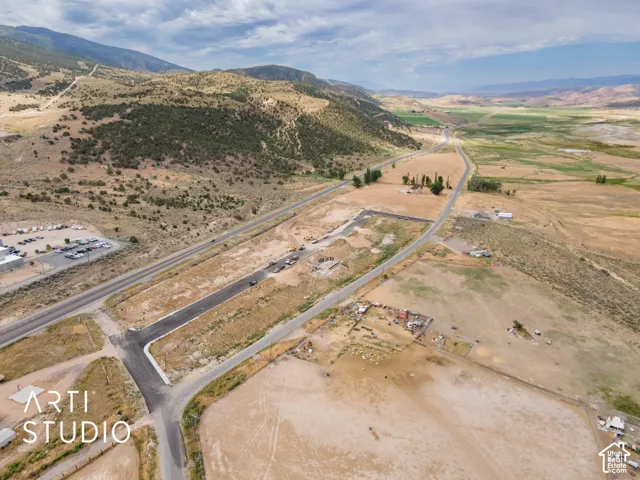 Expansive undeveloped land featuring a paved road, mountainous terrain, and distant green fields