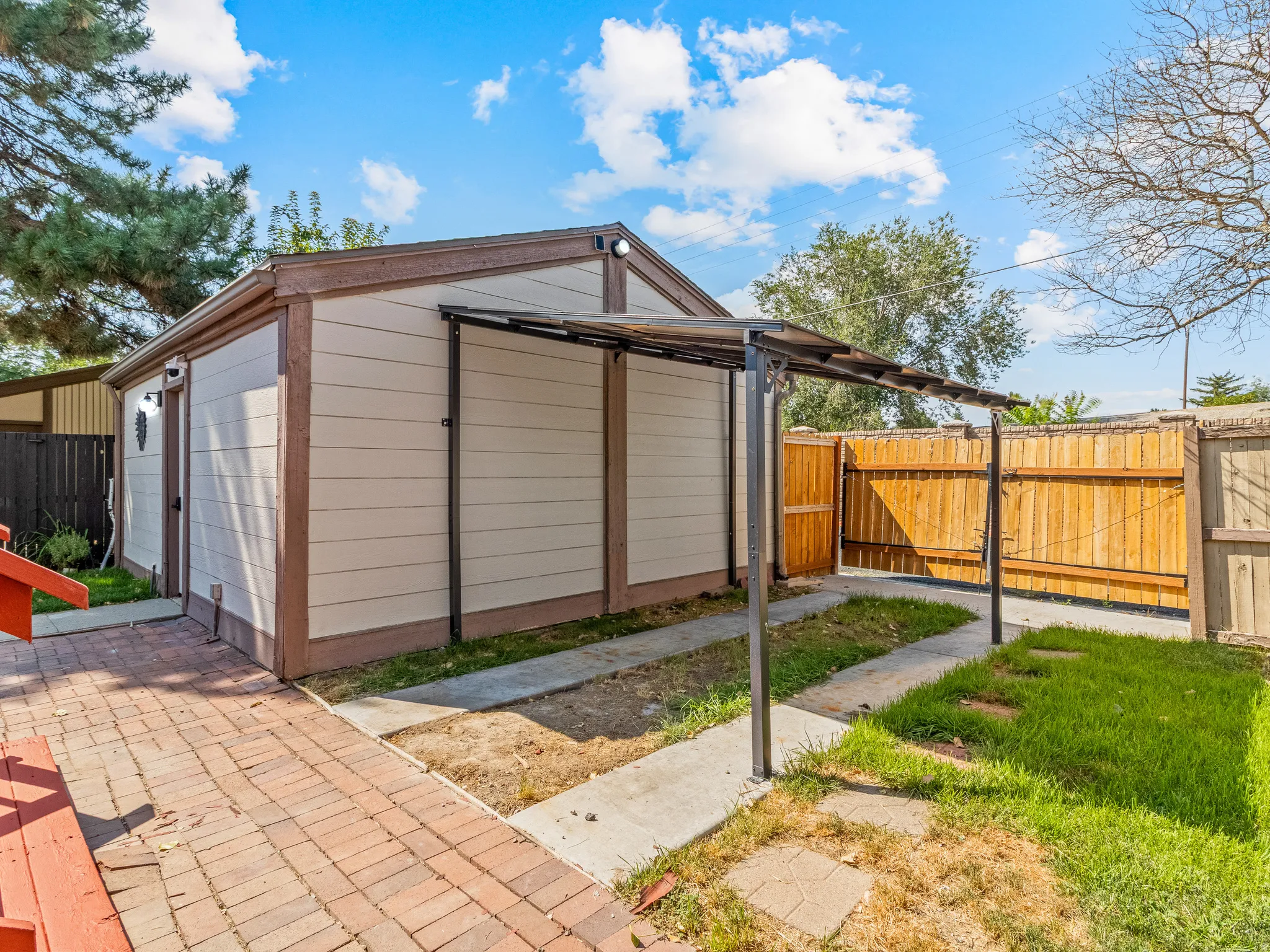 Detached outbuilding with light-toned siding, brown trim, and a covered walkway