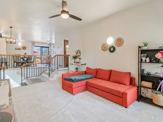 Carpeted main living space with a ceiling fan, a built-in shelving unit, and a split-level design featuring a black wrought iron railing with wood-finish top
