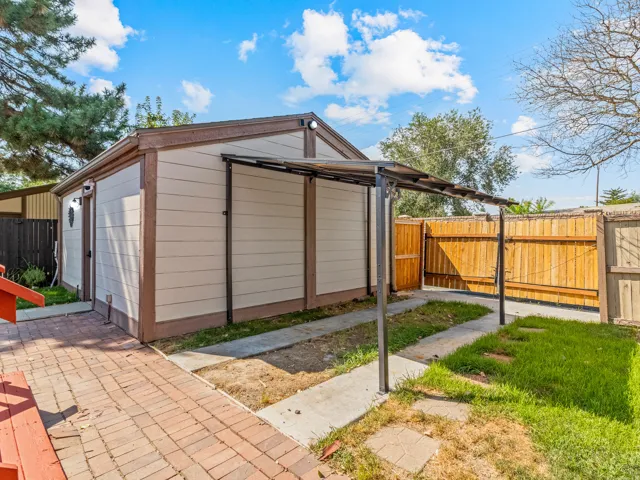 Detached outbuilding with light-toned siding, brown trim, and a covered walkway
