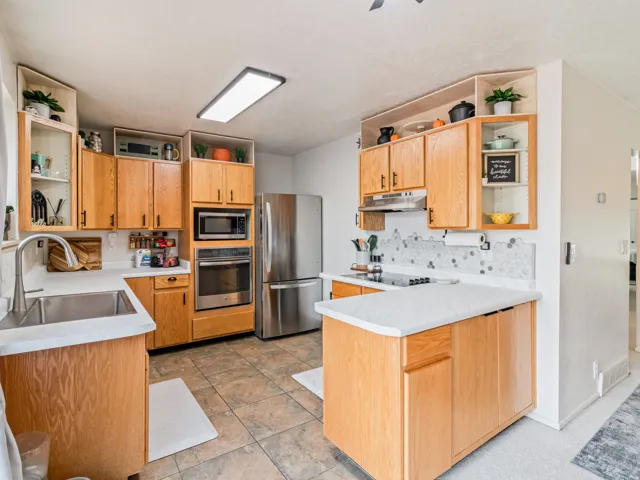 Kitchen featuring wood cabinetry, stainless steel appliances, a kitchen island, tile flooring, and a decorative tile backsplash