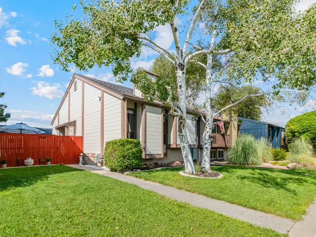 Gable roofline, mature trees, manicured lawn, red privacy fence, and concrete pathway