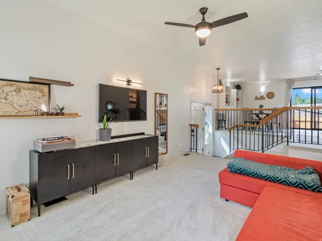 Vaulted ceiling with a ceiling fan, plush carpeting, built-in shelving, and a black metal railing system