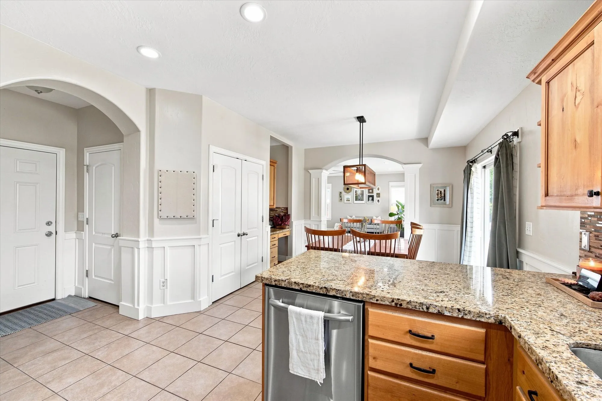 Recessed lighting, wood-finish cabinetry, stainless steel dishwasher, tile flooring, and a stone countertop