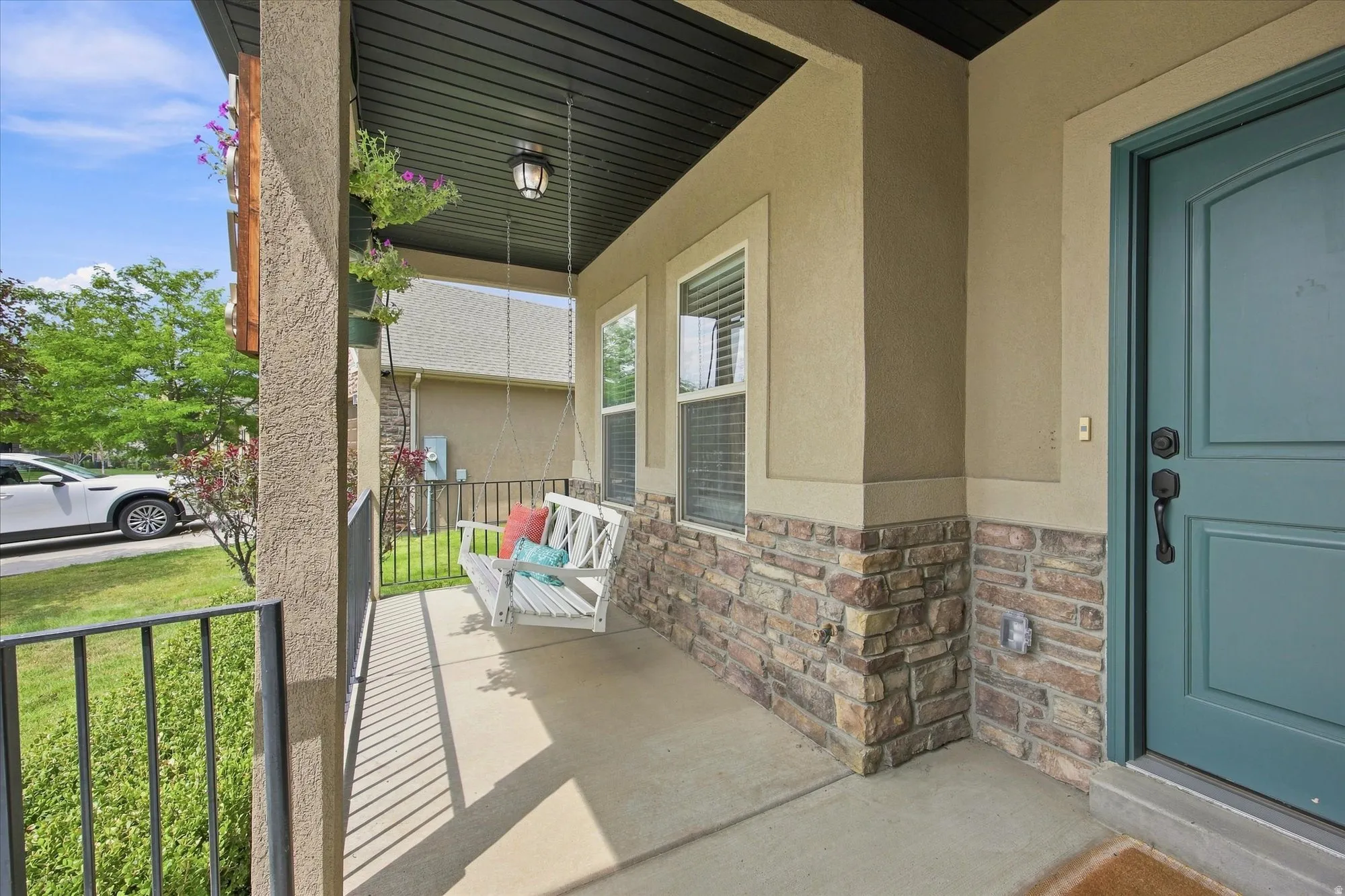 Covered front porch featuring a decorative porch swing, stone facade accents, and a panel-style entry door