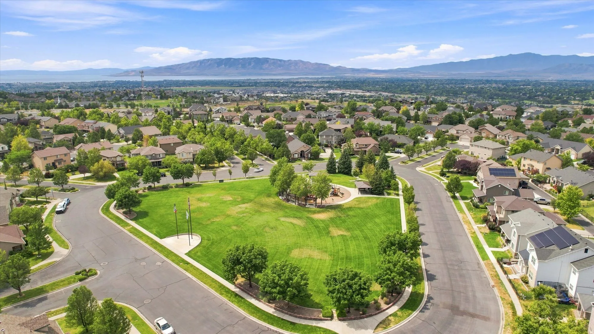 Community green space with mature trees, surrounded by residential properties and paved streets