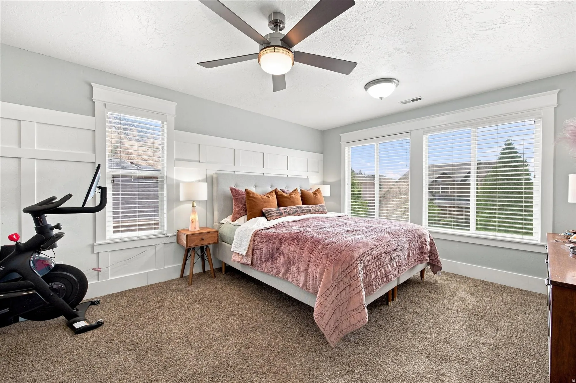 Primary bedroom Carpeted room featuring a ceiling fan with integrated lighting, multiple windows, and board and batten wall detailing