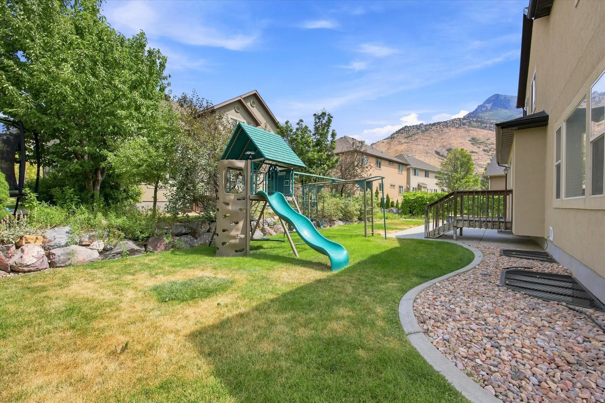 Expansive backyard featuring a manicured lawn, established landscaping, and a wooden deck
