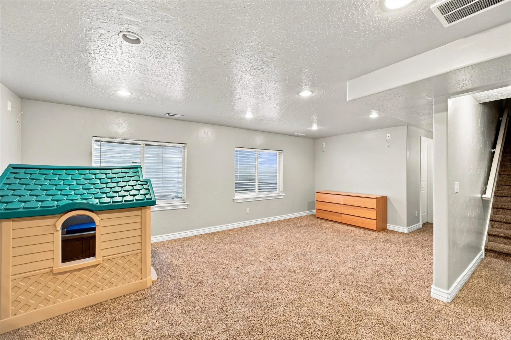 Carpeted room with recessed lighting, multiple windows, and a staircase