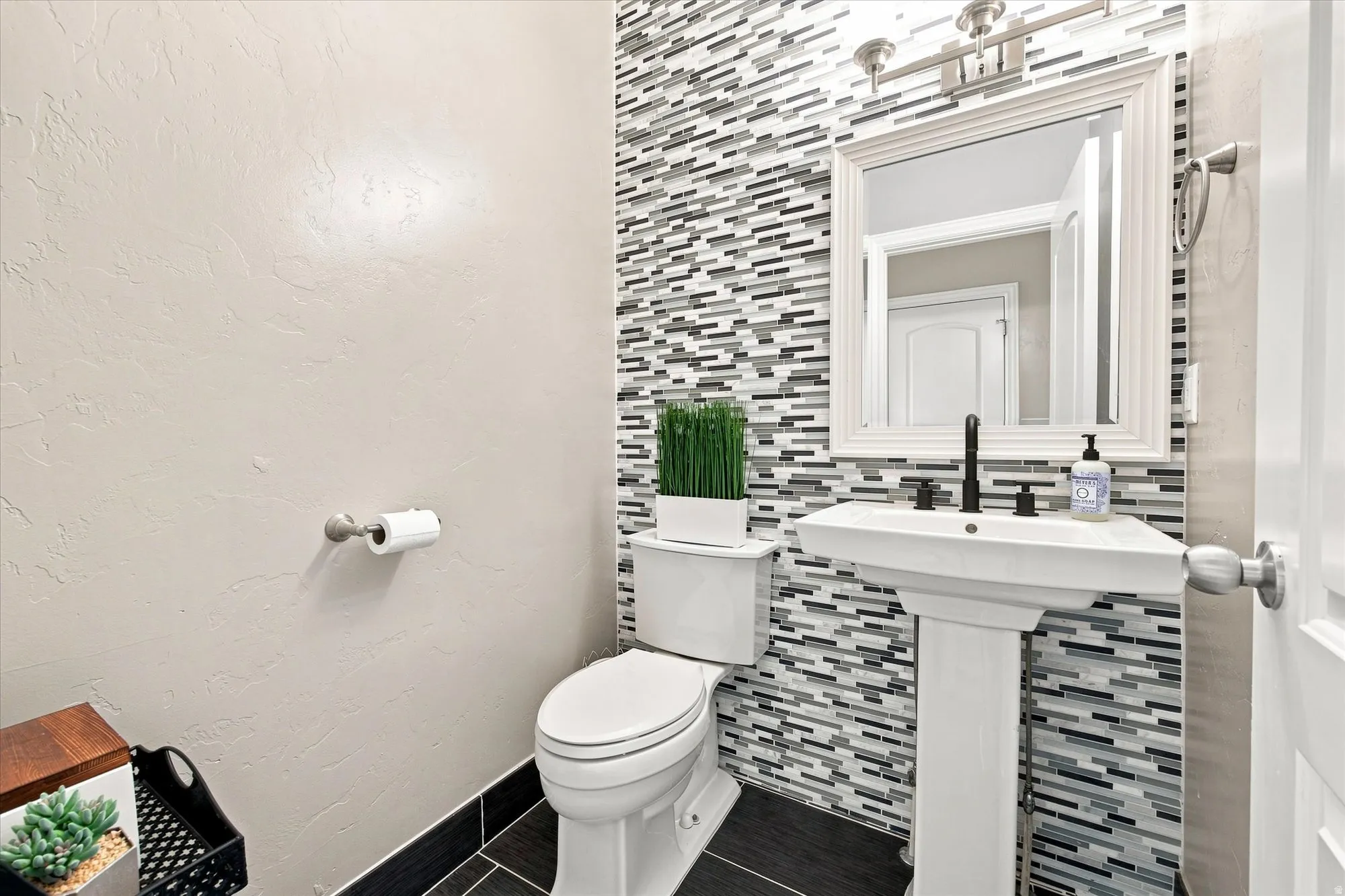 Pedestal sink with matte black faucet, wall-mounted mirror, and decorative tile accent wall