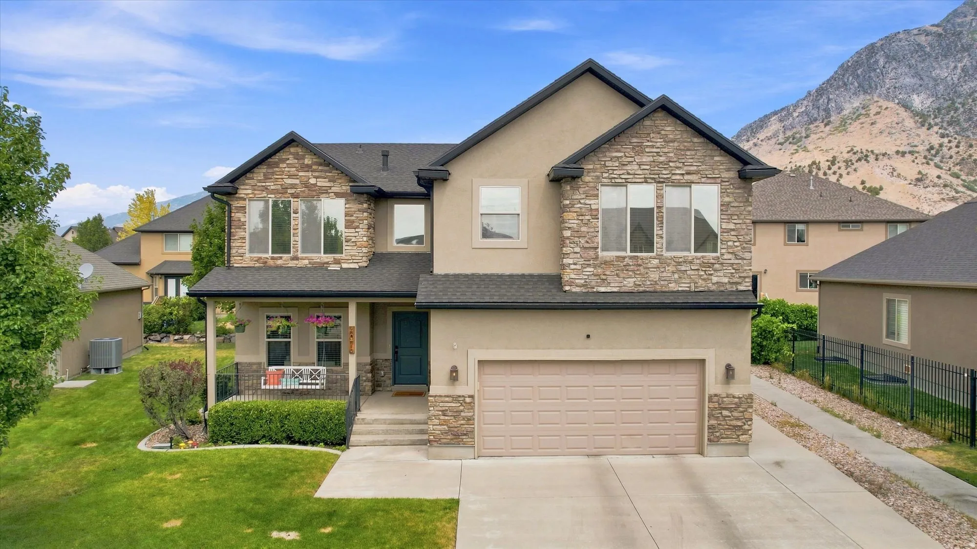 Stucco and stone facade with an attached garage, covered front porch, and a well-maintained lawn