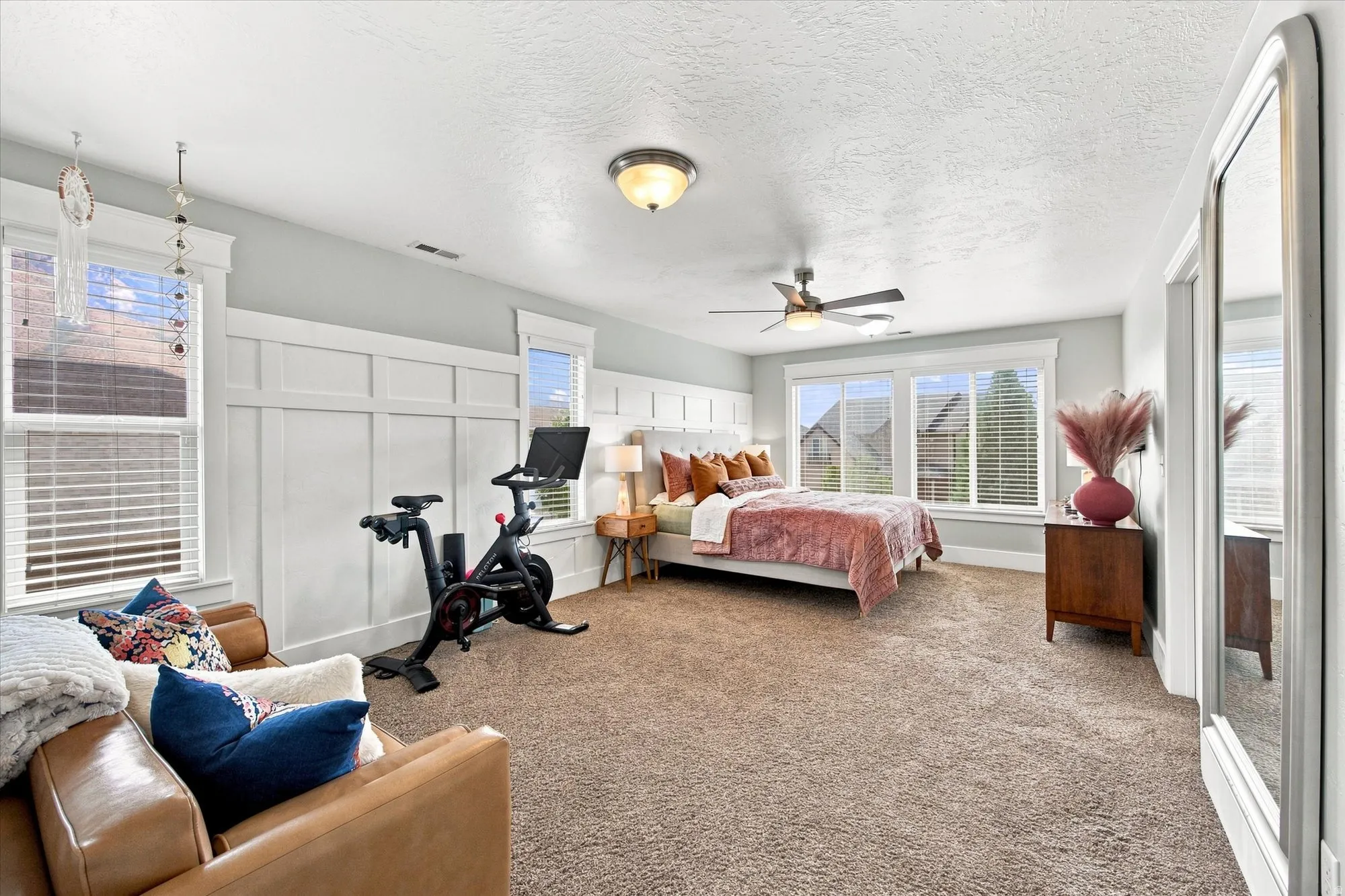 Primary bedroom Spacious room featuring carpeted flooring, a ceiling fan, multiple windows with blinds, and decorative wainscoting
