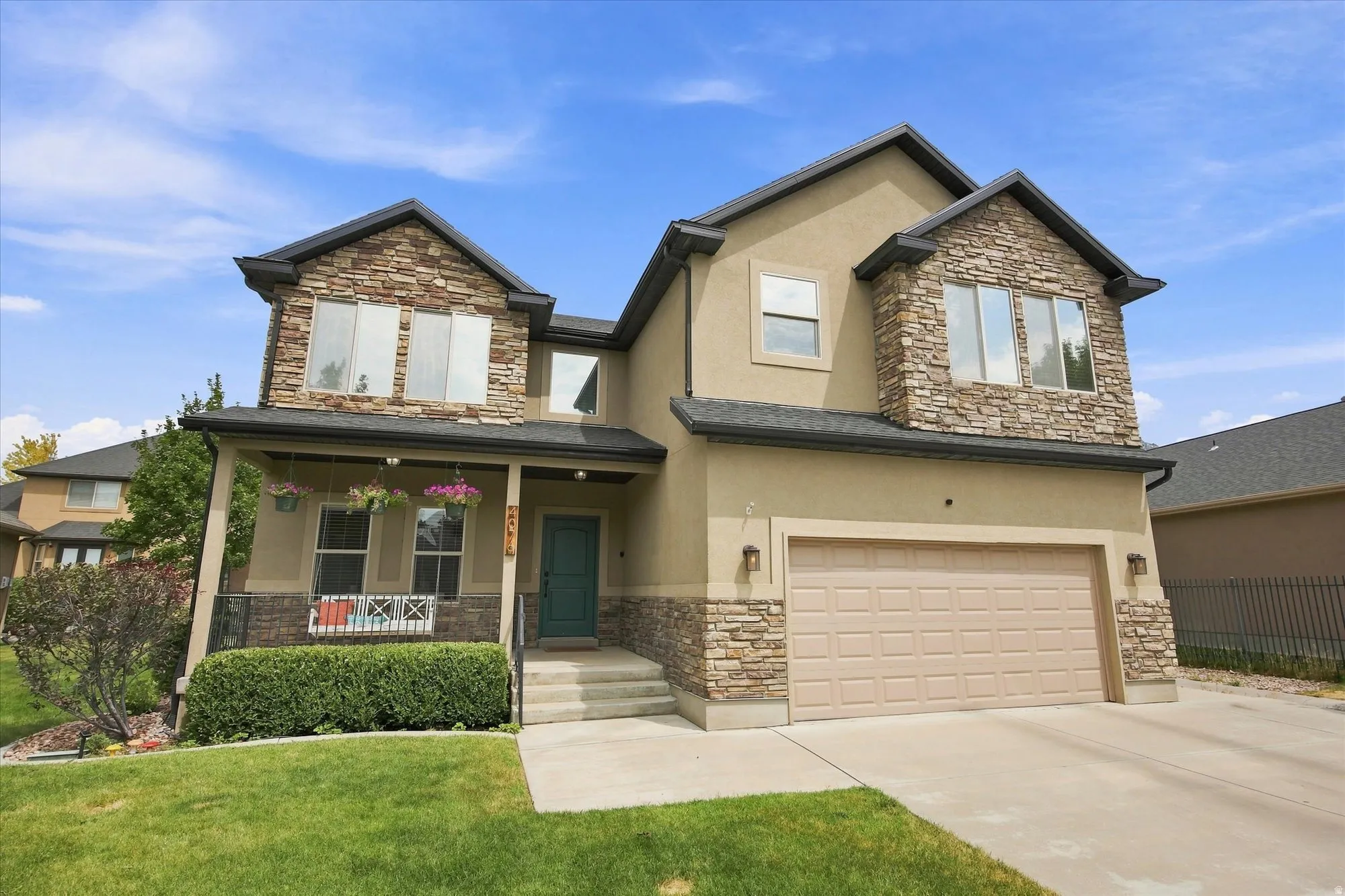 Stucco exterior with stone accents, covered front porch, attached garage, and concrete driveway