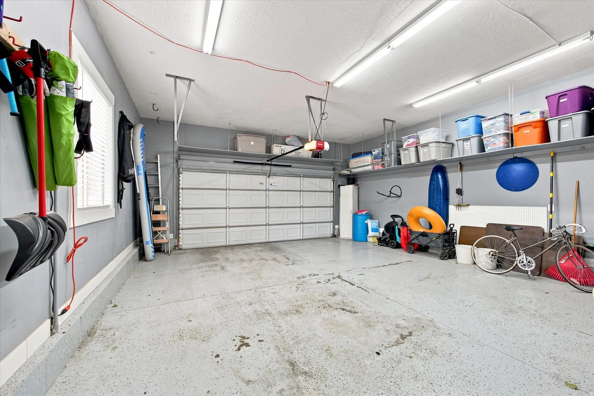 Spacious garage featuring a sectional garage door, overhead fluorescent lighting, a window with blinds, and built-in wall shelving