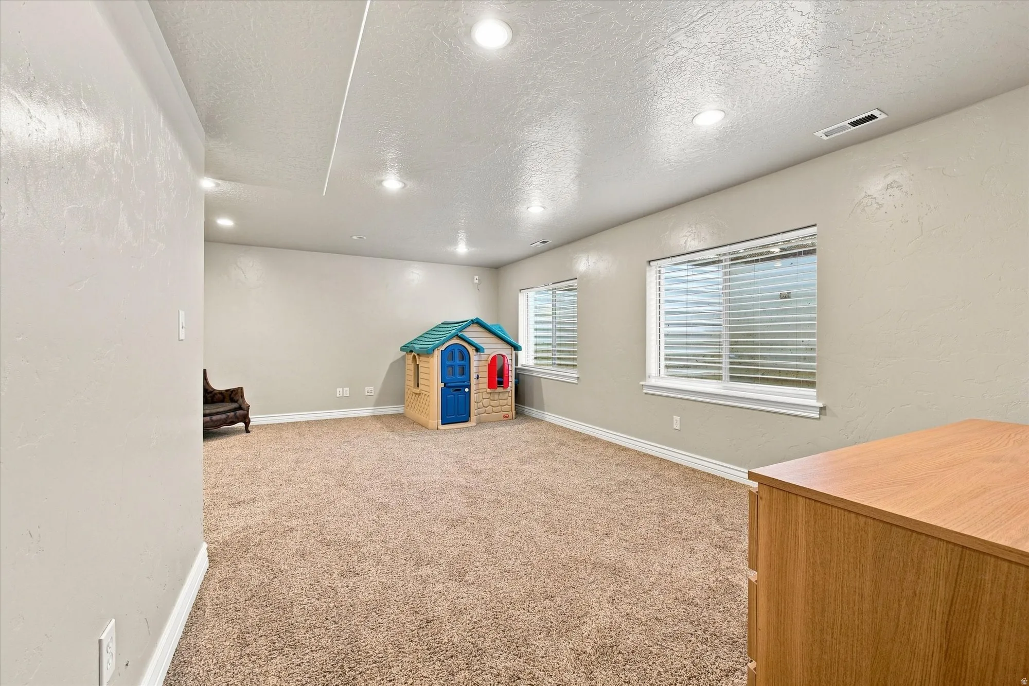 Recessed lighting, light beige wall paint, carpeted flooring, two windows with blinds, and white trim