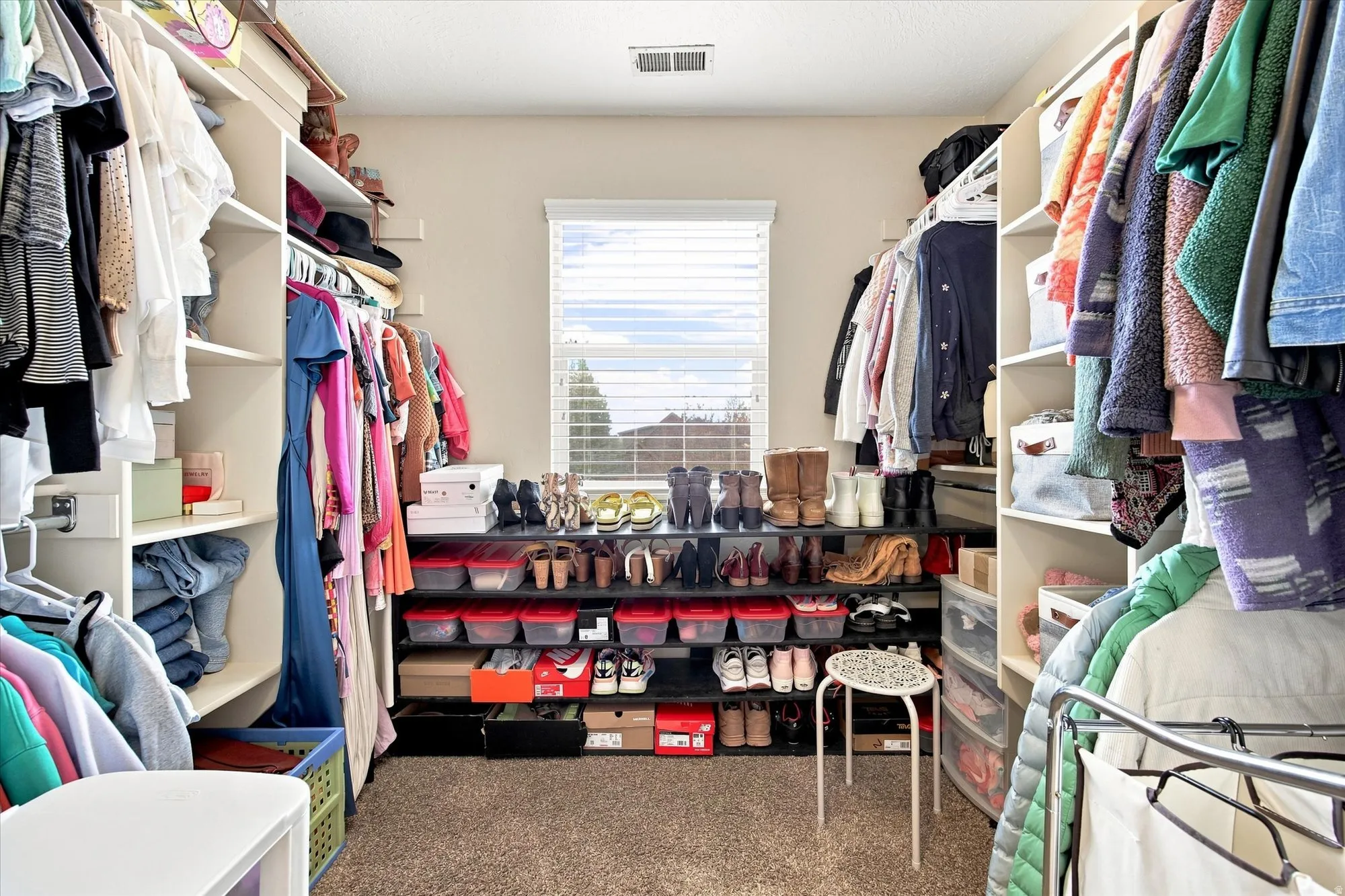 Primary bedroom closet, window with horizontal blinds, built-in shelving, and clothes hanging rods