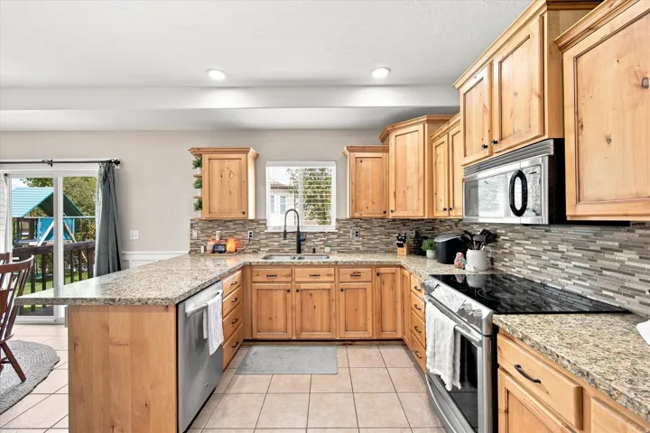U-shaped kitchen with wood-finish cabinetry, granite countertops, tile flooring, and a mosaic tile backsplash