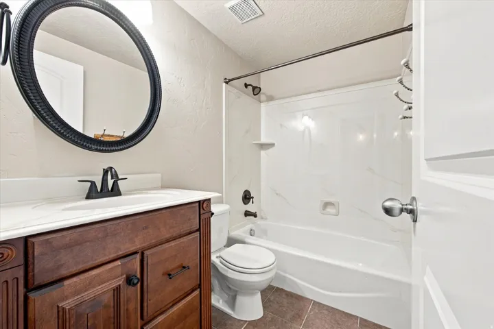 Wood vanity with dark hardware, white countertop, and an oval mirror