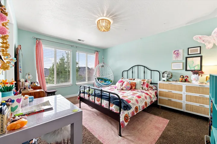Dual windows with blinds, wall-mounted decorative light fixture, wrought iron bed frame, six-drawer dresser with cane accents, and soft wall tones