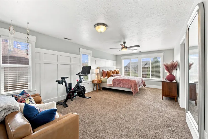 Primary bedroom Spacious room featuring carpeted flooring, a ceiling fan, multiple windows with blinds, and decorative wainscoting