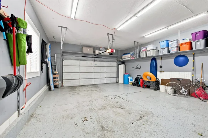 Spacious garage featuring a sectional garage door, overhead fluorescent lighting, a window with blinds, and built-in wall shelving