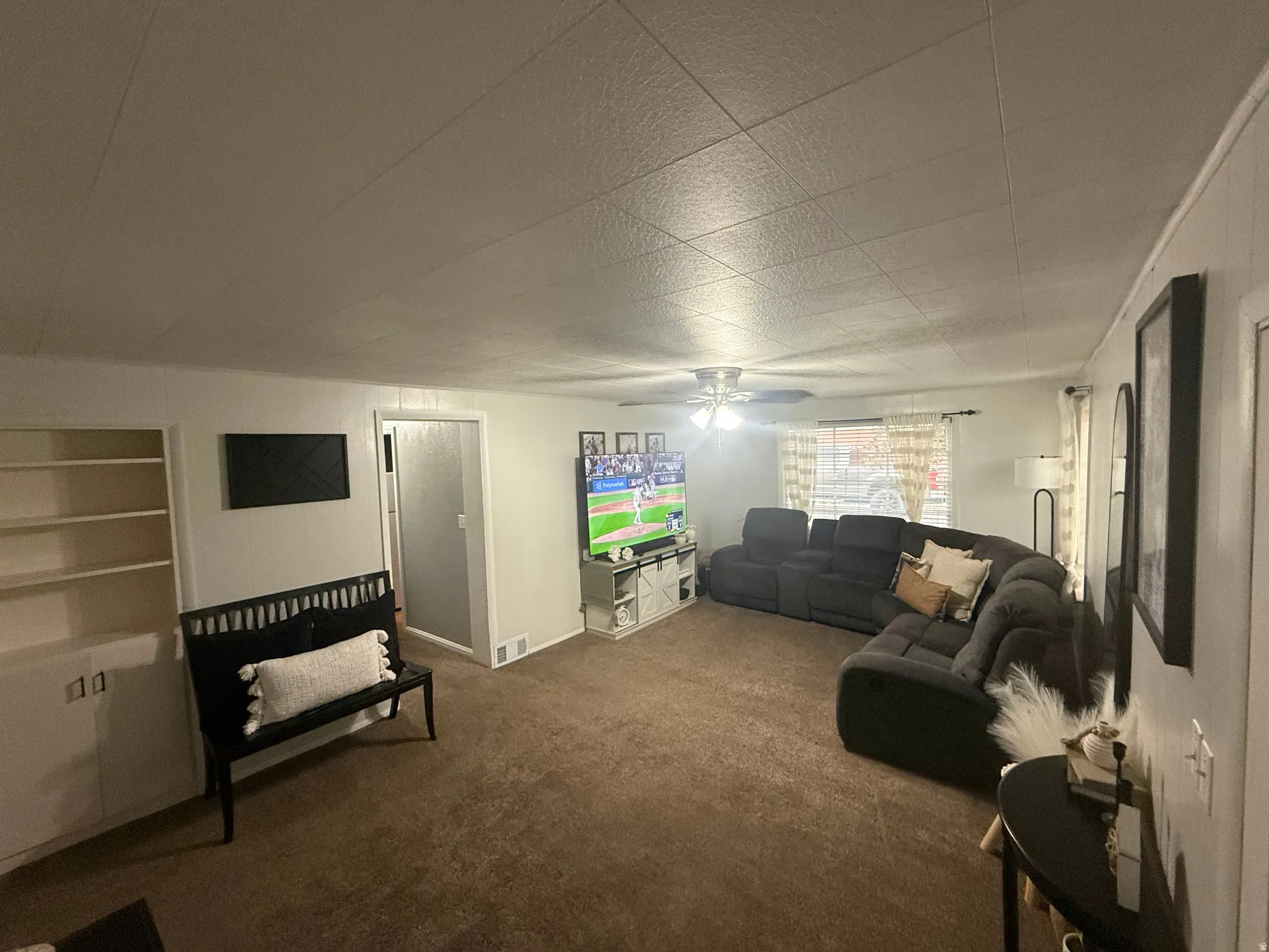 Living area with wall-to-wall carpeting, built-in shelving, paneled walls, and a ceiling fan