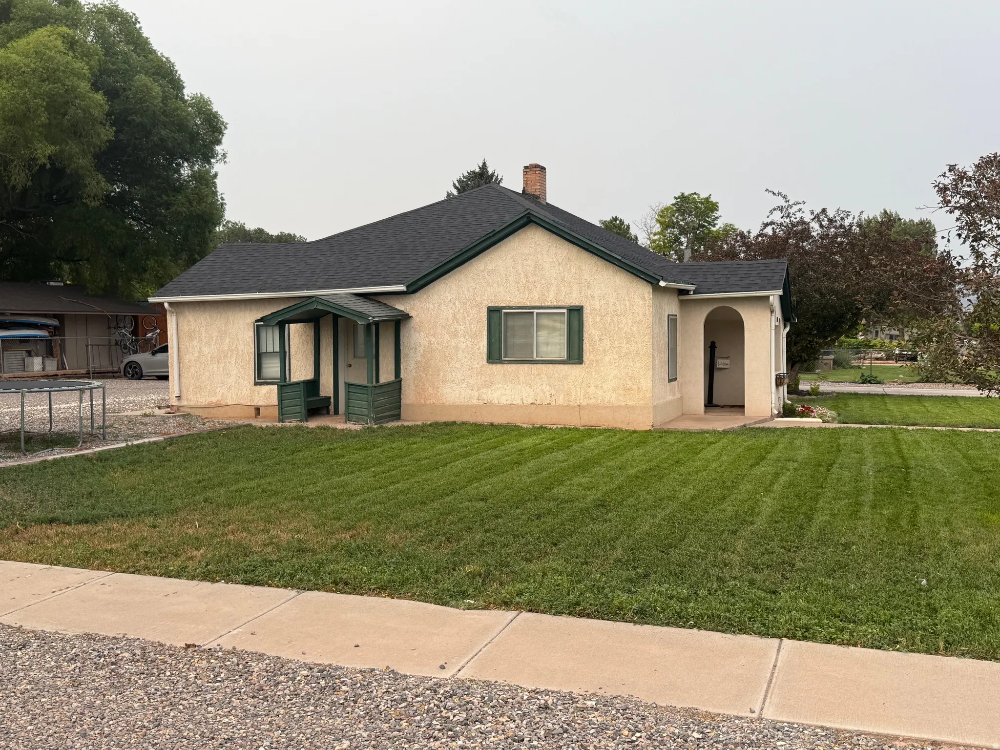 Stucco exterior with a dark shingle roof, featuring a covered front porch and a secondary arched entryway