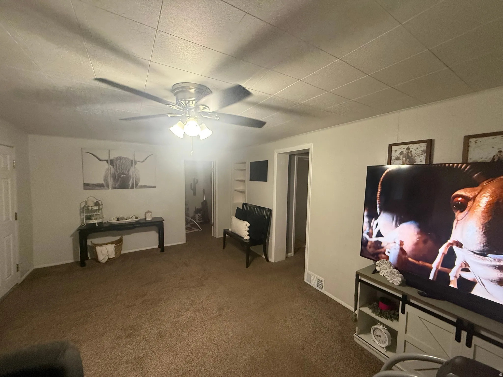 Neutral wall color, ceiling fan with integrated lighting, built-in shelving, carpet flooring, and a barn door-style media console