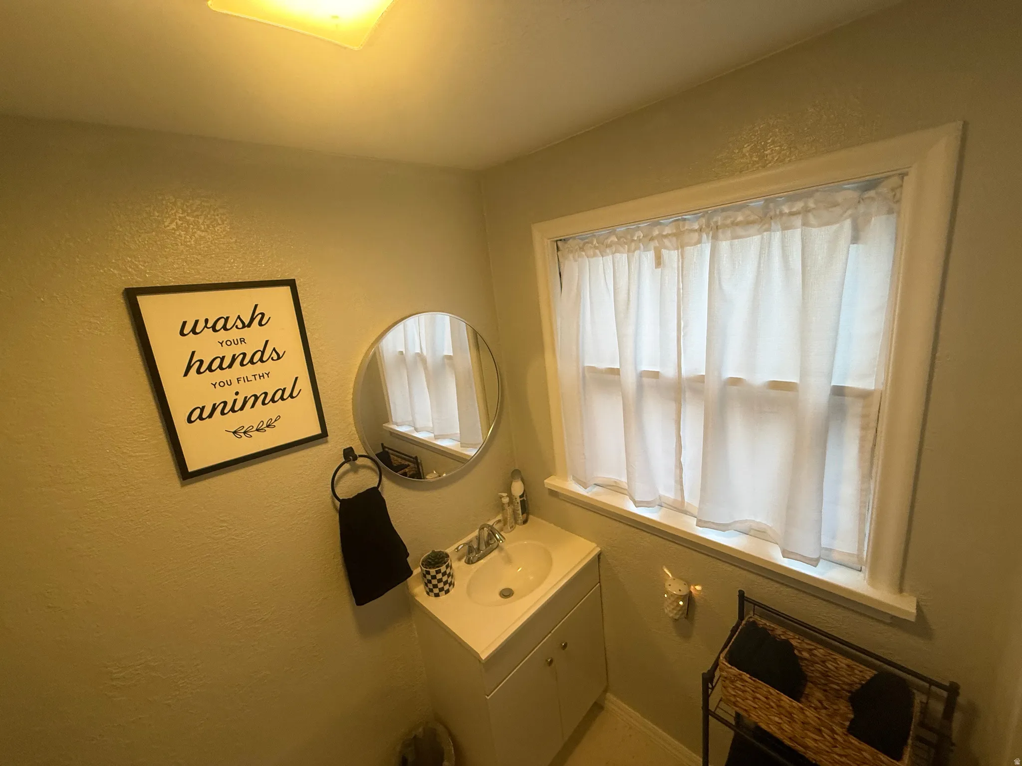 Single window with white trim, wall-mounted circular mirror, white vanity with integrated sink, and overhead lighting fixture