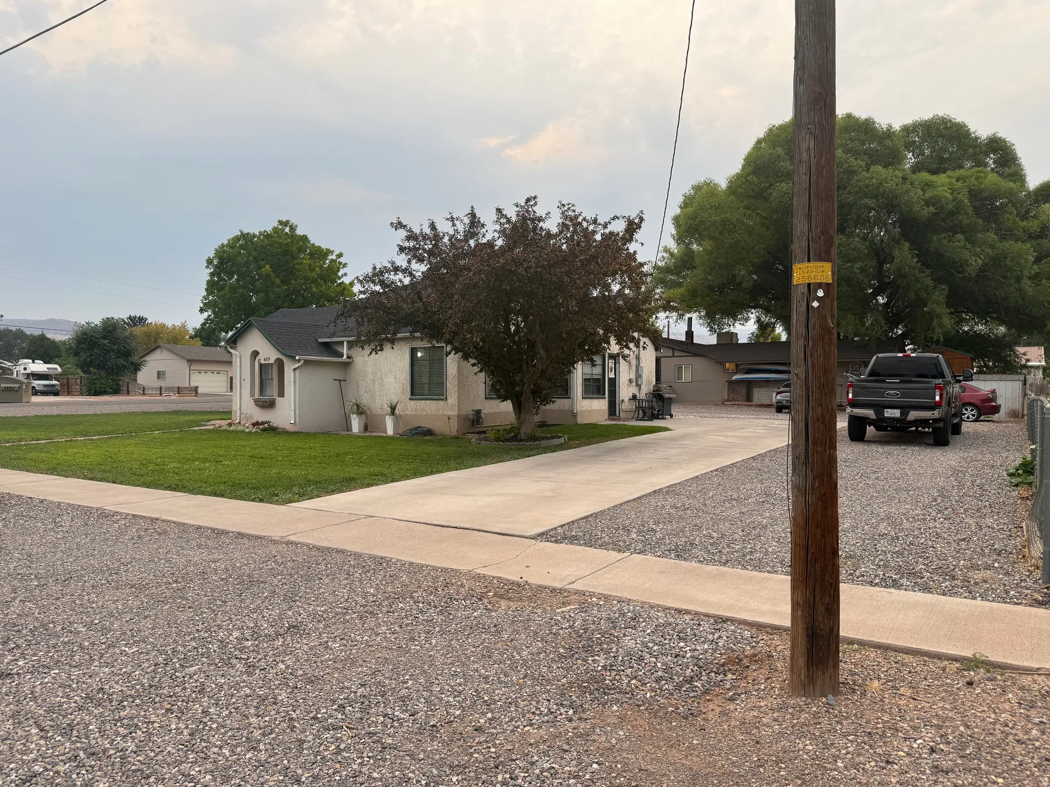 Stucco exterior residence with a composition shingle roof, established lawn, concrete driveway, and gravel parking area