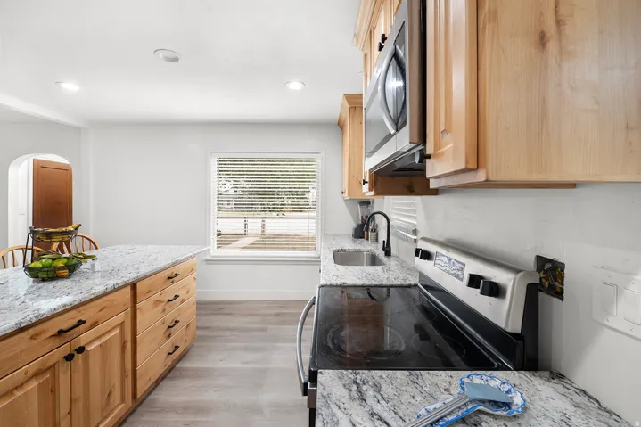 Kitchen featuring wood cabinetry, stainless steel appliances, granite countertops, and wood-finish flooring