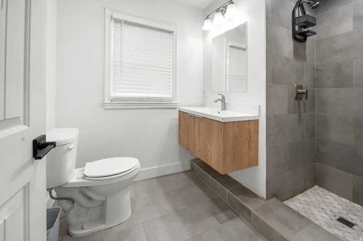 Floating wood-finish vanity with an integrated sink, tiled shower with a niche, wall-mounted showerhead, and a white toilet