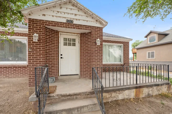 Brick exterior featuring a covered entry, white paneled door with windowpanes, and decorative wrought iron railings