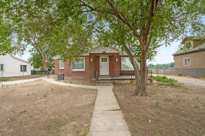 Brick-clad exterior with a white entry door, covered porch, and mature trees