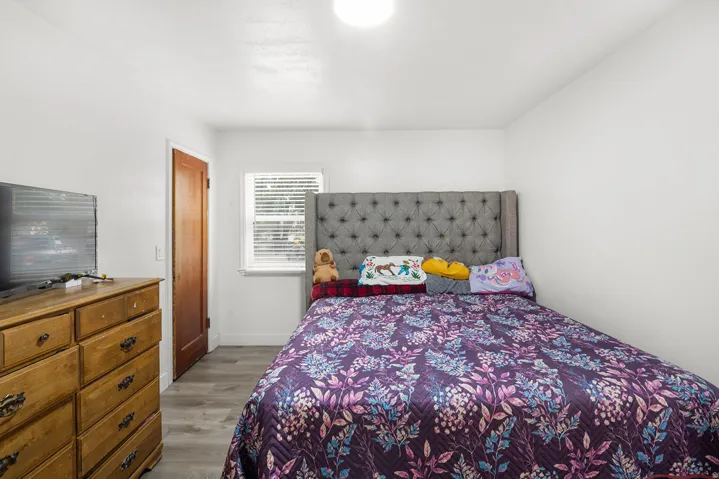 Wood-finish flooring, white walls, wood panel door, and a window with blinds
