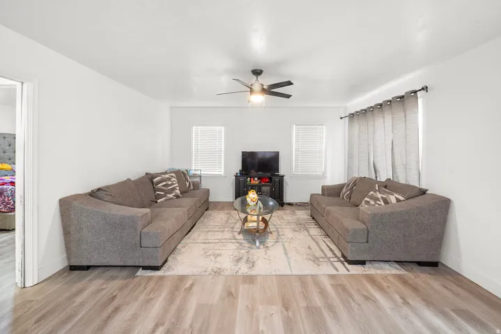 Wood-finish flooring throughout, white walls, two windows with blinds, and a ceiling fan with integrated lighting