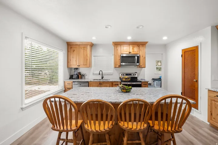 Central island with stone-finish countertop, wood-finish cabinetry, stainless steel appliances, wood-finish flooring, and recessed lighting