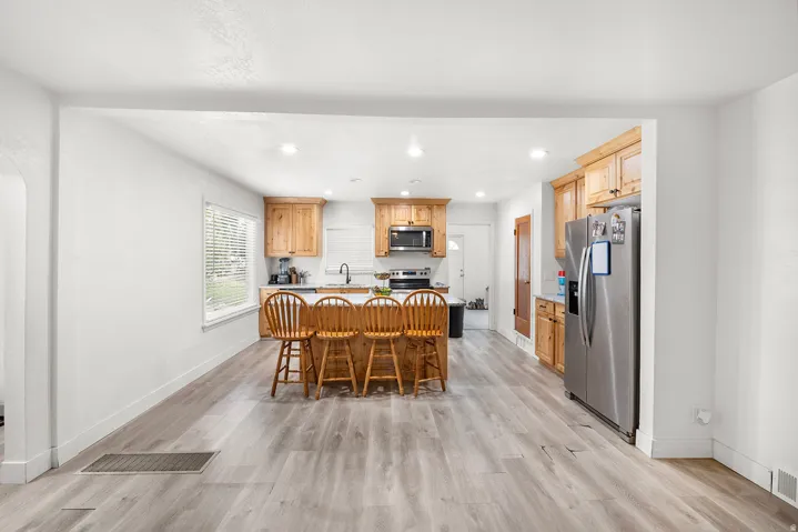 Open-concept kitchen with wood-finish flooring, recessed lighting, wood cabinetry, stainless steel appliances, and a central island with countertop seating