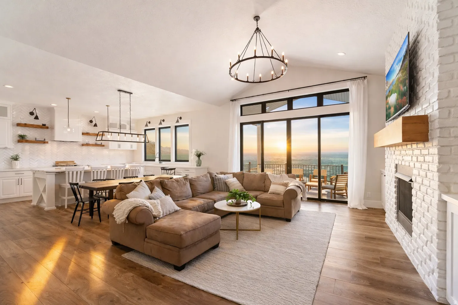 Open-concept living space featuring a large sectional arrangement, hardwood flooring throughout, and expansive glass sliding doors opening to a covered balcony with scenic outlooks