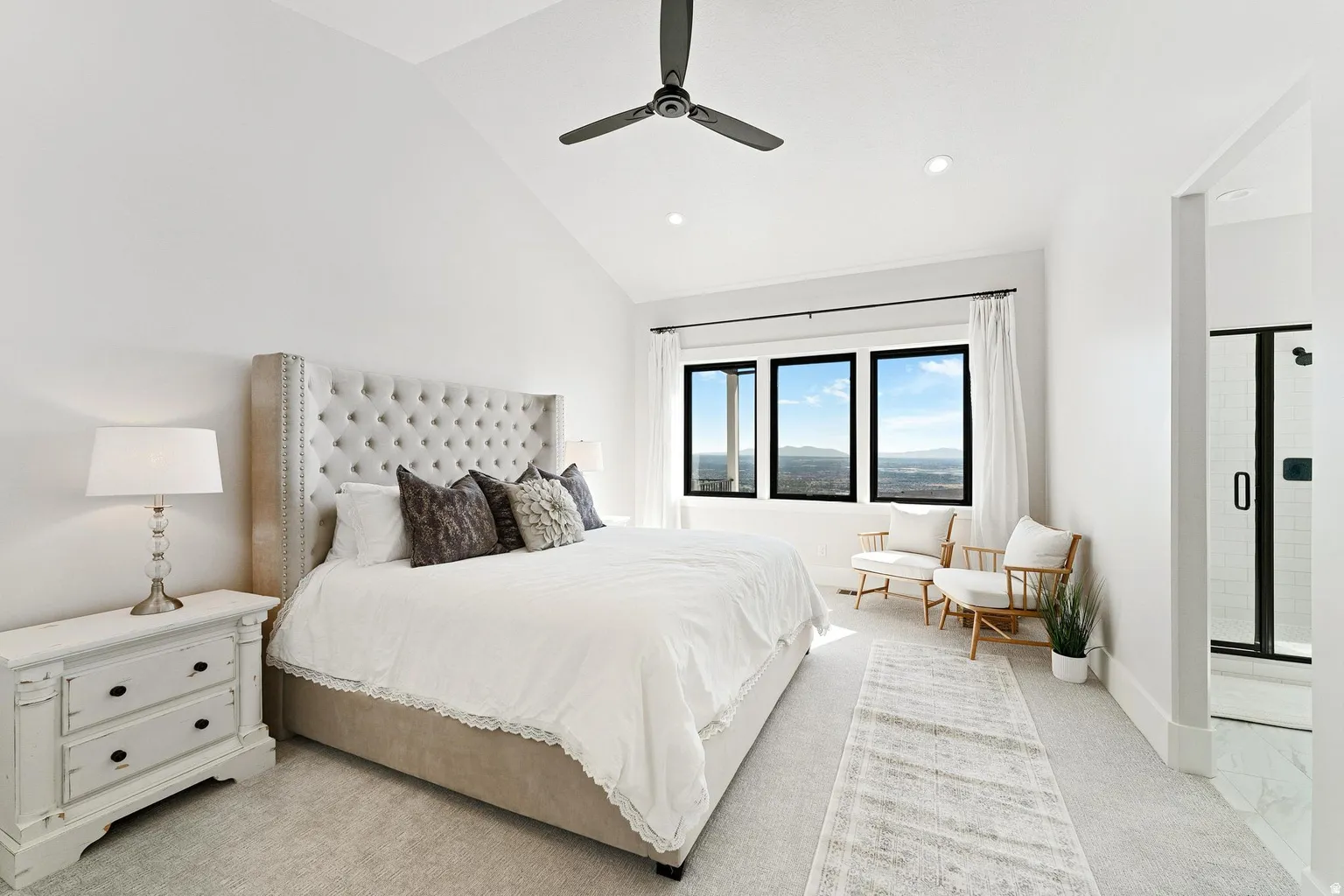 Bright primary bedroom featuring a tufted upholstered headboard, recessed ceiling lighting, ceiling fan, and triple casement windows flooding the space with natural light