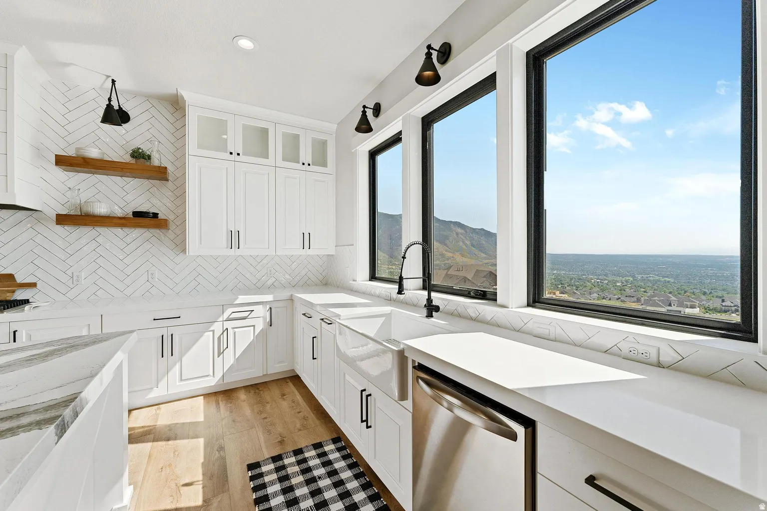 White shaker-style cabinetry with matte black hardware, herringbone tile backsplash, integrated farmhouse sink, stainless steel dishwasher, and wood-finish flooring