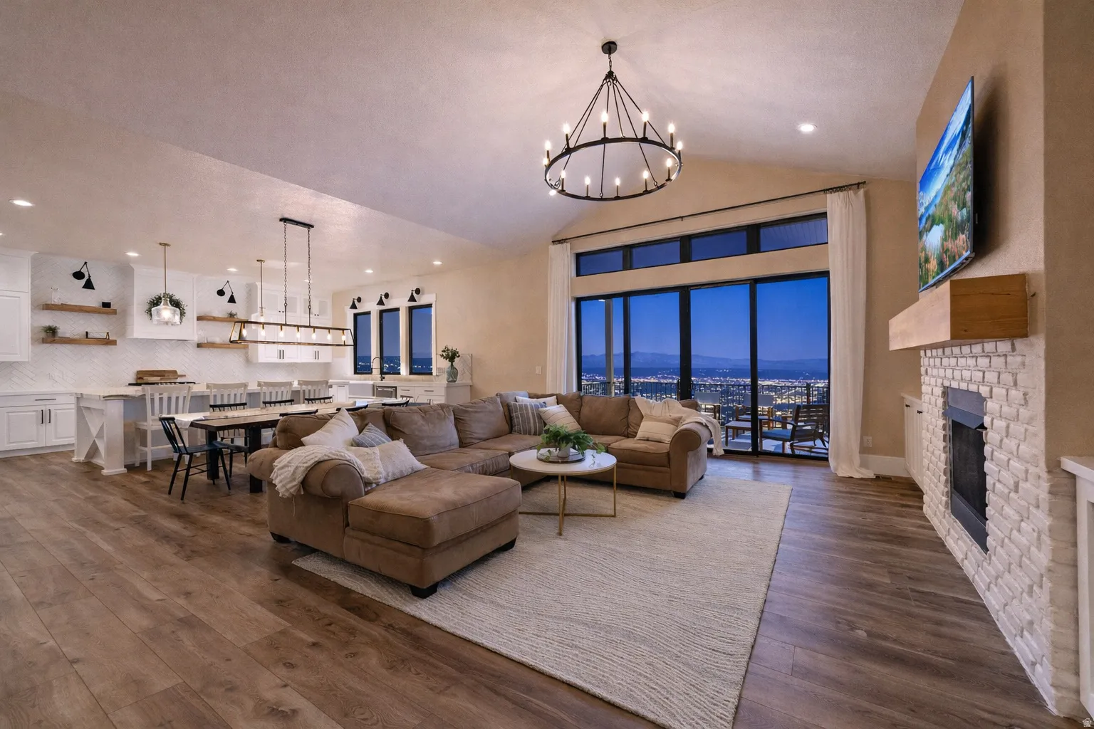 Open-concept living space featuring wood-finish flooring, a white brick fireplace with a wood mantel, and expansive glass sliding doors