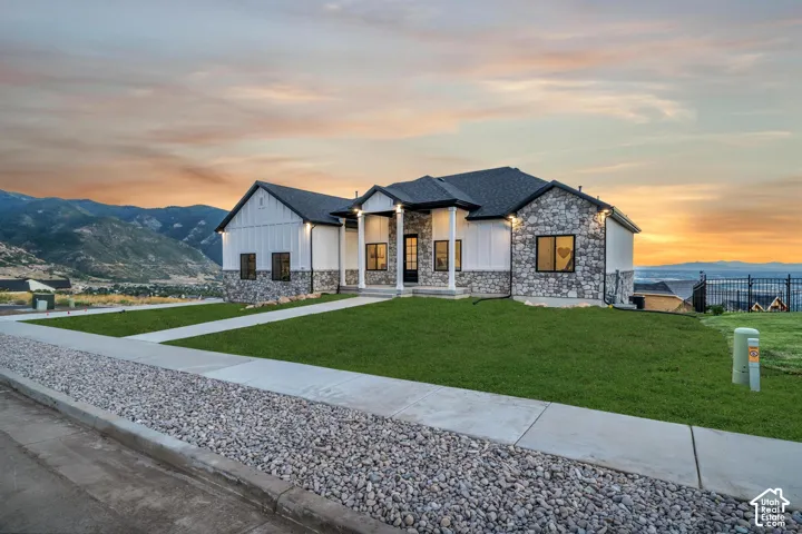 Modern exterior with stone accents, vertical white siding, a dark shingle roof, and a manicured lawn