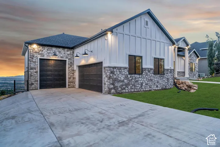 Stone and board-and-batten exterior with a dark-pitched roof, concrete driveway, and attached two-car garage